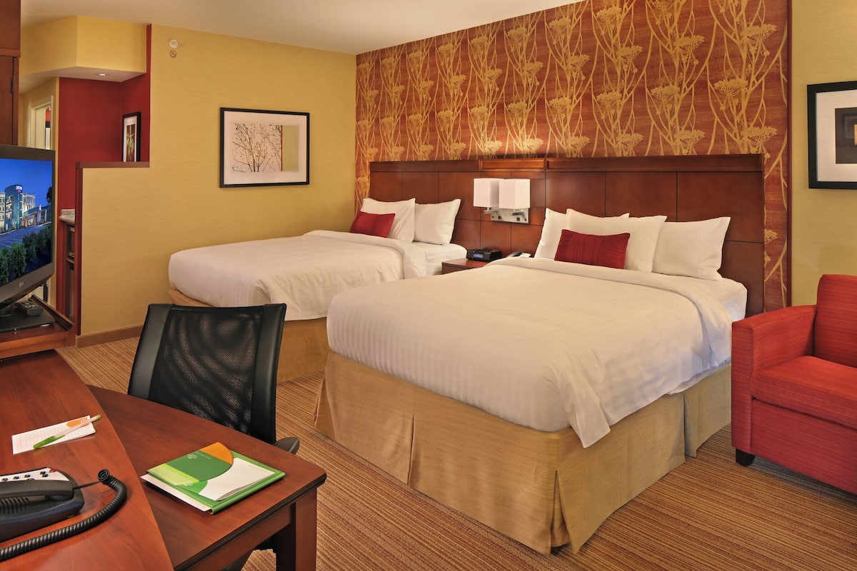 A hotel room with two beds, a desk with a telephone, a chair, and a television.