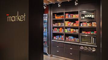Un área de cocina con microondas, refrigerador y estantes llenos de aperitivos y bebidas.