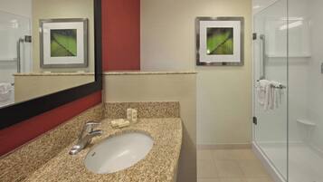 A modern bathroom with a granite countertop, a white sink, a mirror, and a glass-enclosed shower.