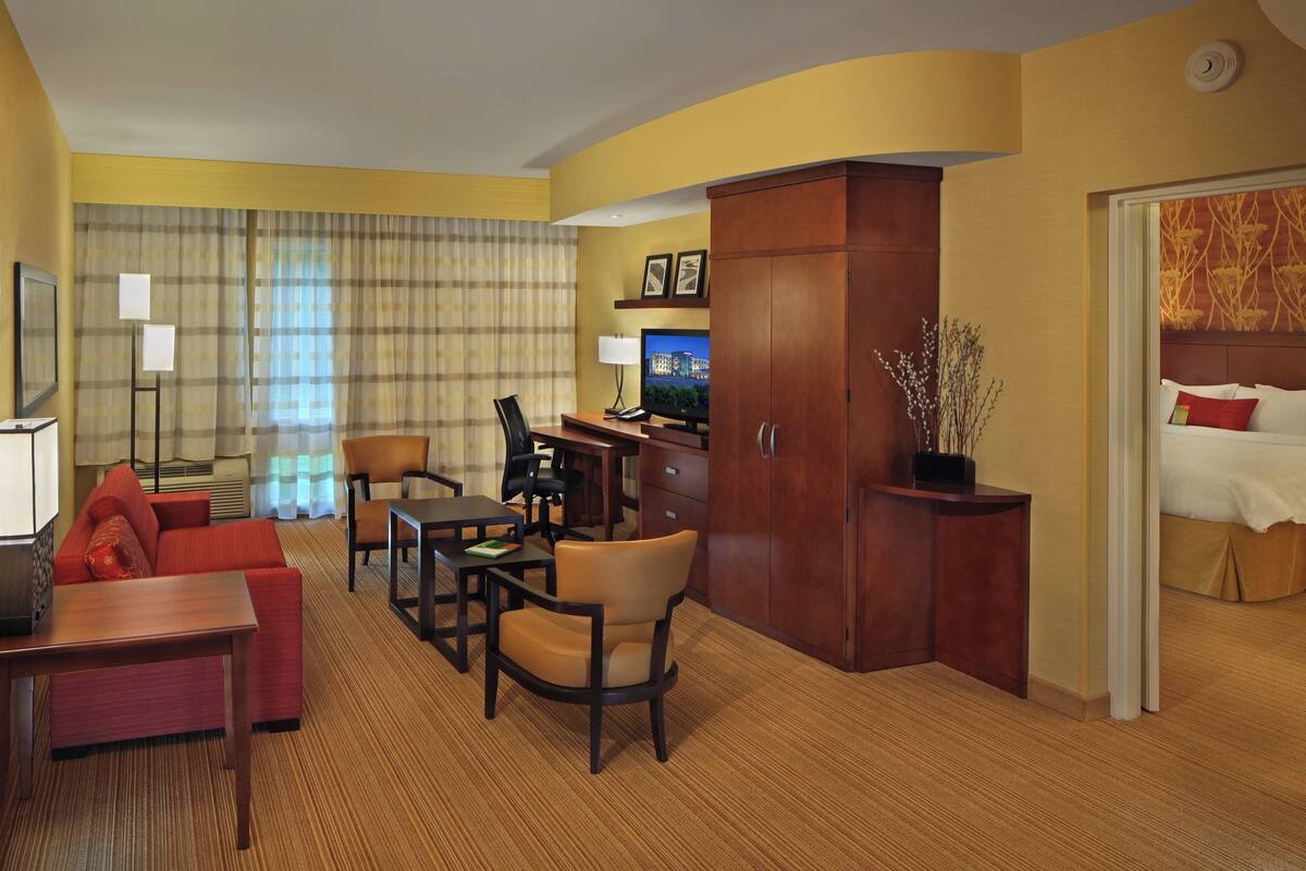 A hotel room with a bed, a desk, a chair, a sofa, and a television.