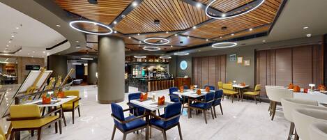 Un restaurante moderno con barra, techo de madera y una mezcla de sillas azules y amarillas.