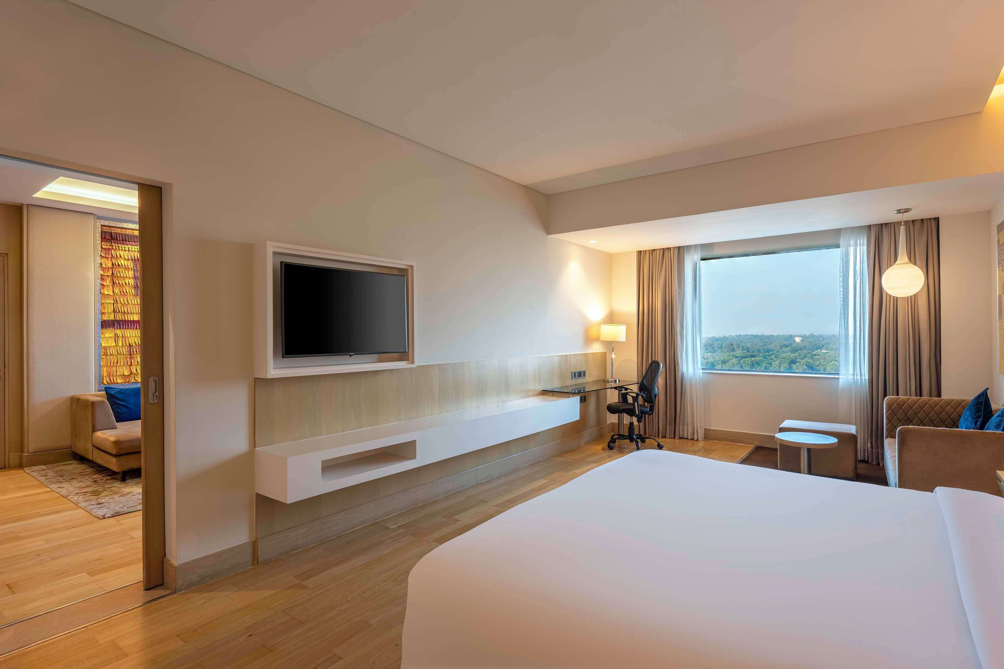 Ein Hotelzimmer mit einem großen Bett, einem an der Wand befestigten Fernseher, einem Schreibtisch mit Stuhl und einem Fenster mit Aussicht.