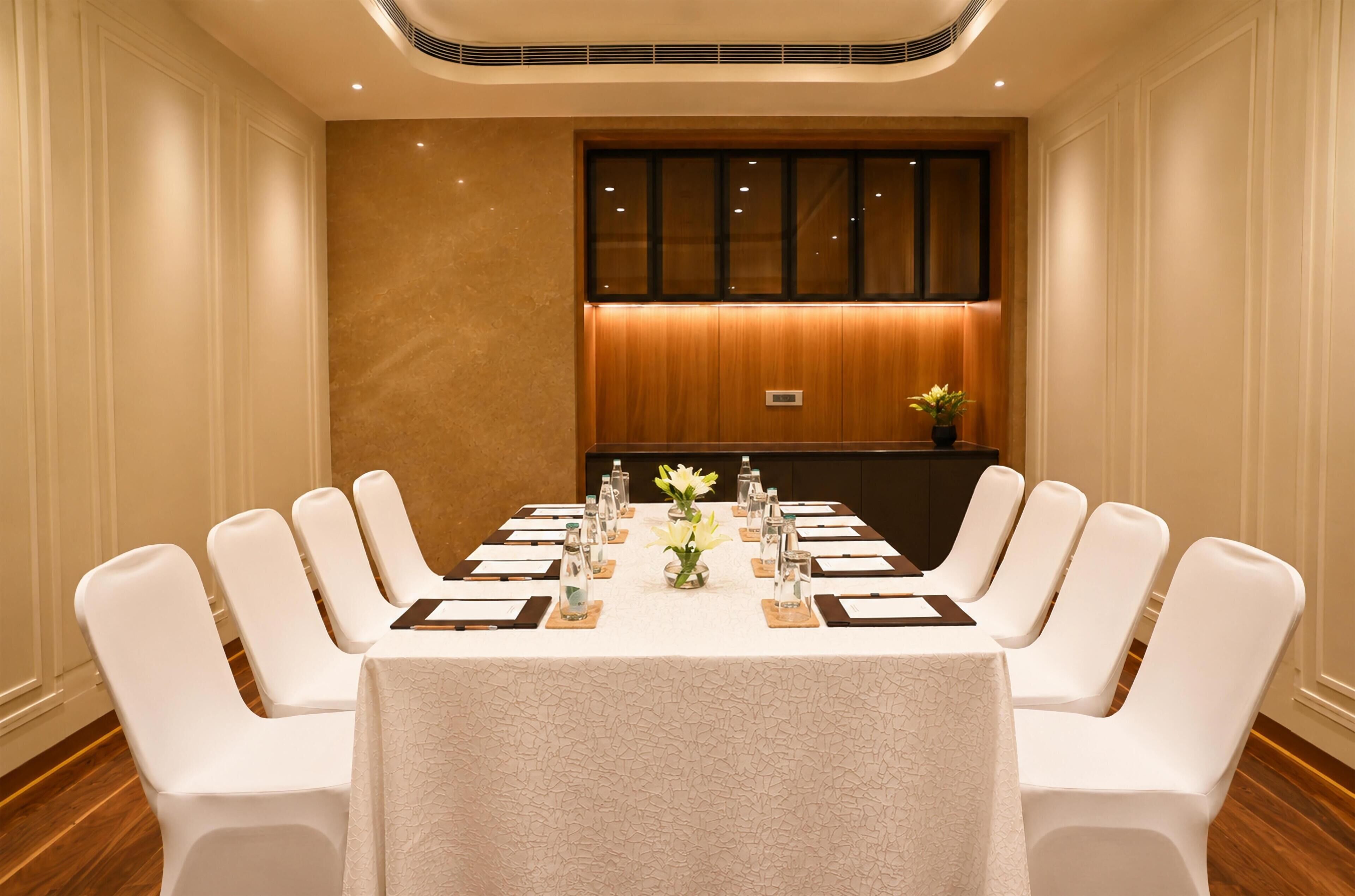 Une salle de conférence avec une longue table, des chaises blanches et un mur recouvert de panneaux en bois.