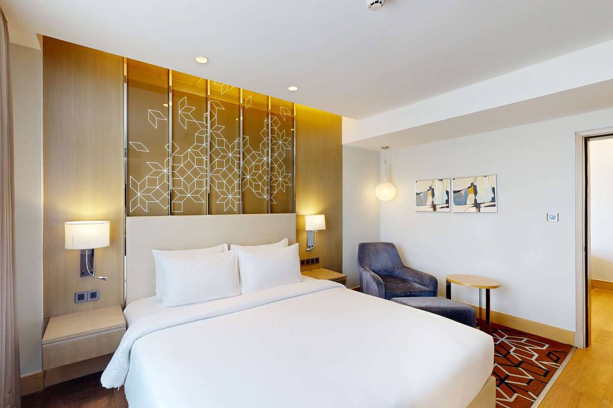 Ein Hotelzimmer mit einem großen Bett, zwei Nachttischlampen, einem Sessel, einem kleinen Tisch und einer Zierleiste an der Wand.