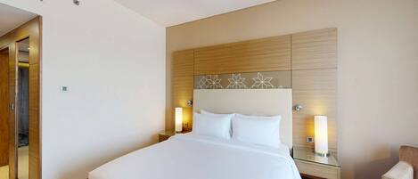 A modern hotel room with a large bed, two bedside tables with lamps, a wooden headboard with geometric patterns, and a mirror on the left wall.