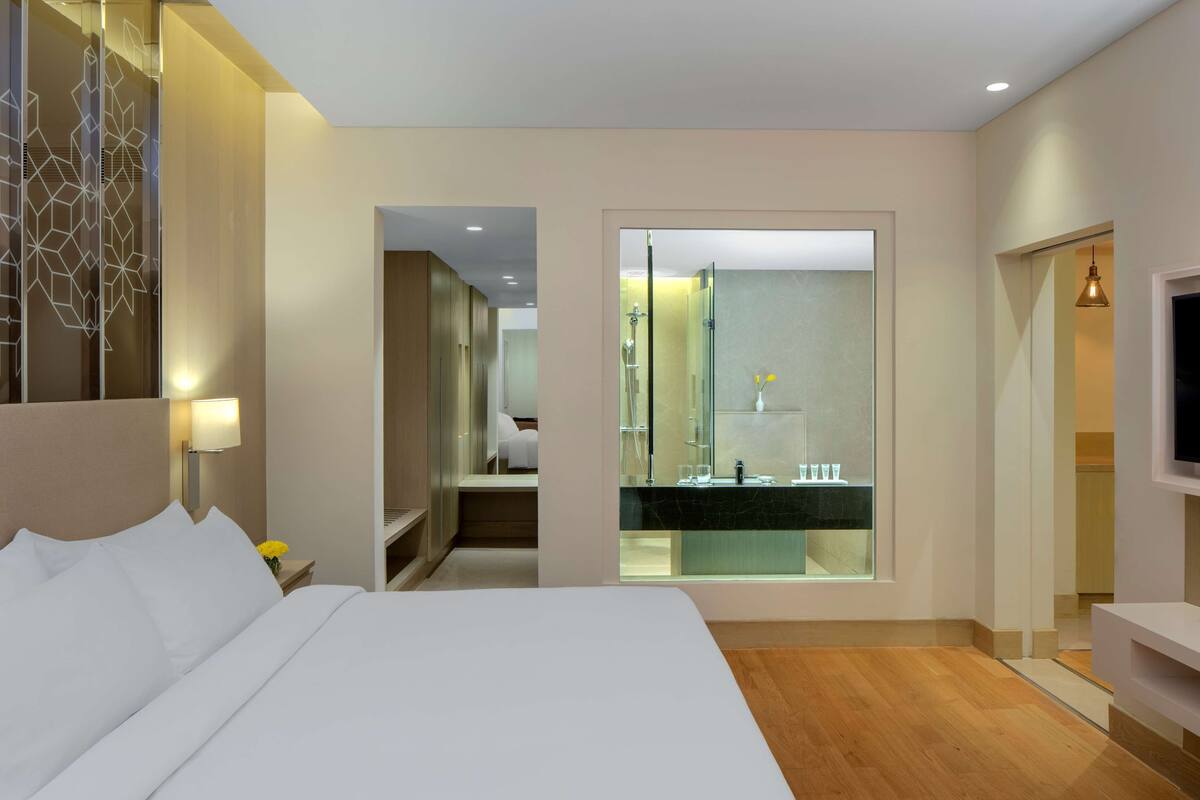 Ein modernes Hotelzimmer mit einem großen Bett, einem Fernseher, einem Badezimmer mit Glasabtrennung und Holzboden.