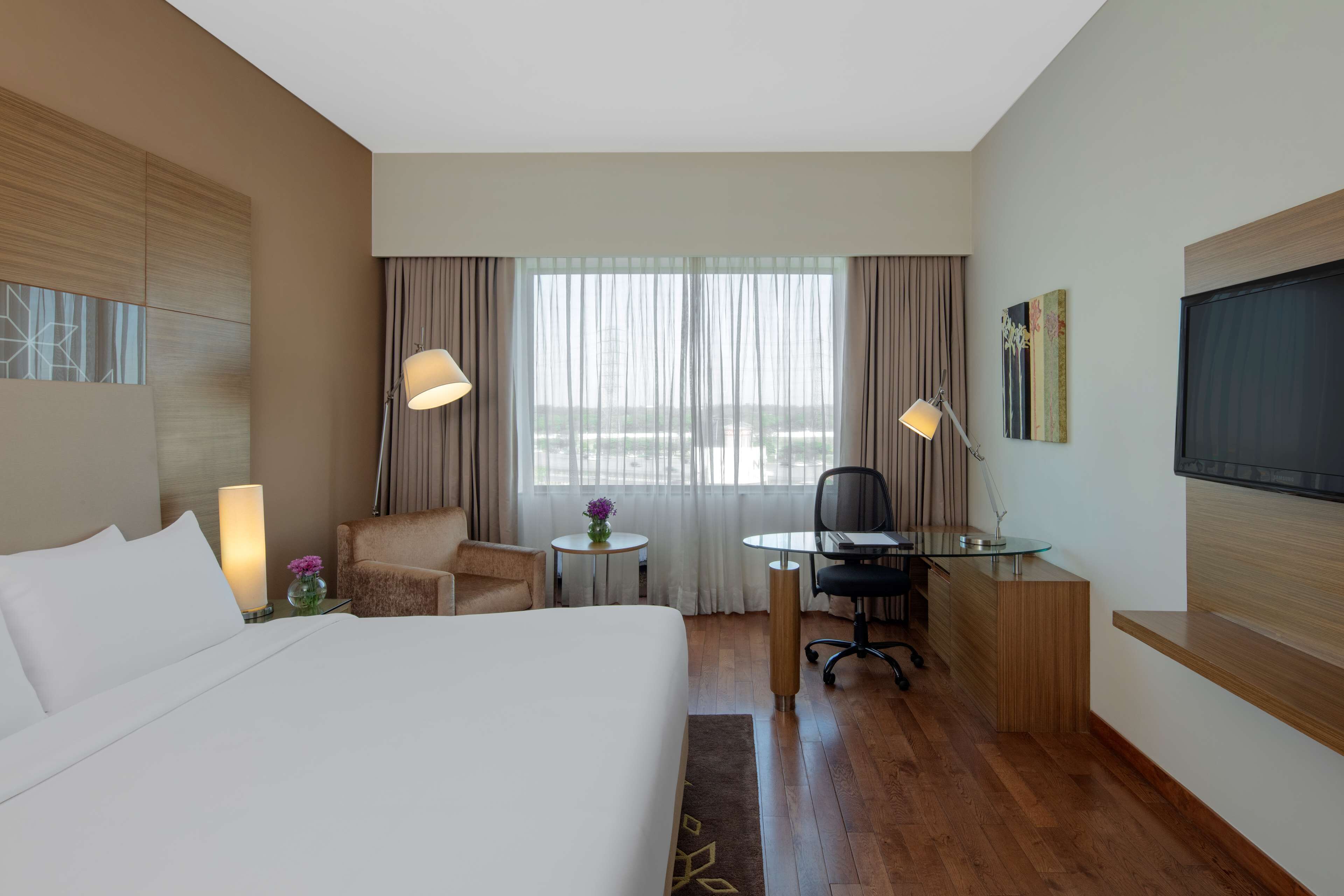 Habitación de hotel con una cama grande, un escritorio con una silla, una mesita con un florero y un televisor en la pared.