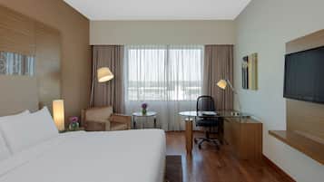Habitación de hotel con una cama grande, un escritorio con una silla, una mesita con un florero y un televisor en la pared.
