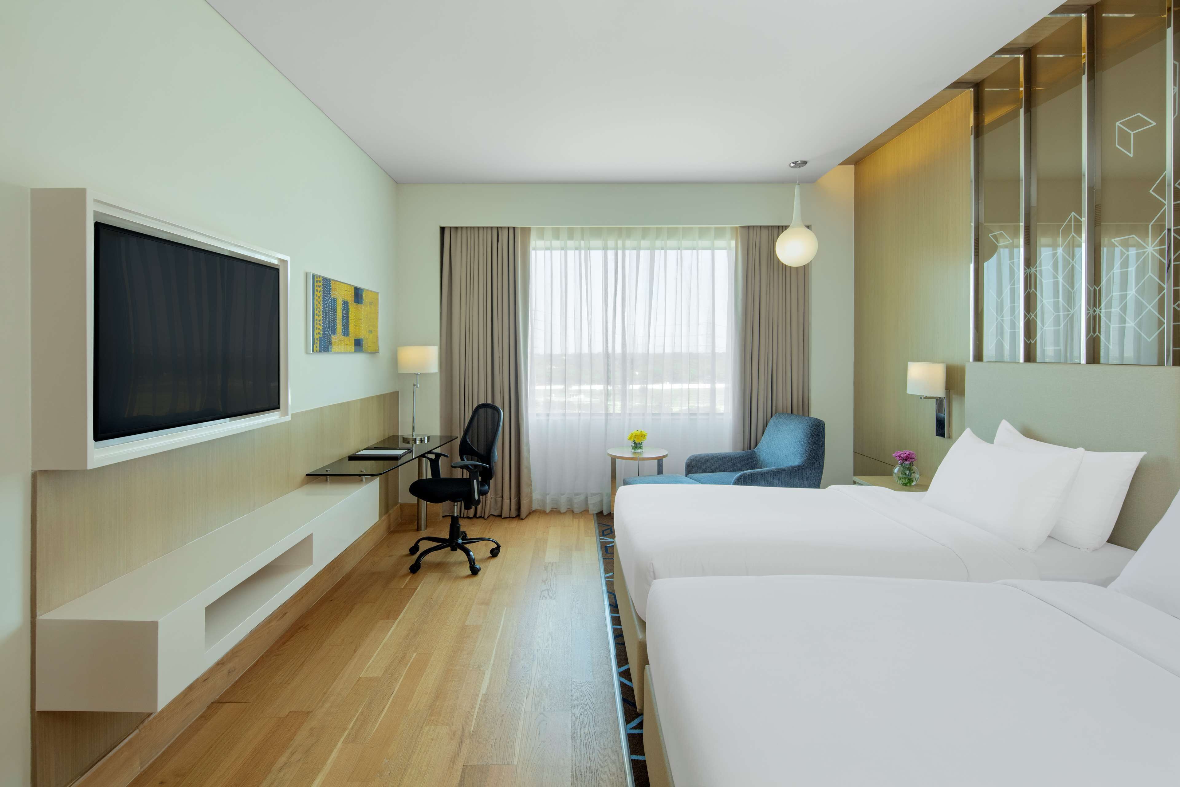 Habitación de hotel con dos camas, un escritorio, una silla, un televisor y una ventana con cortinas.