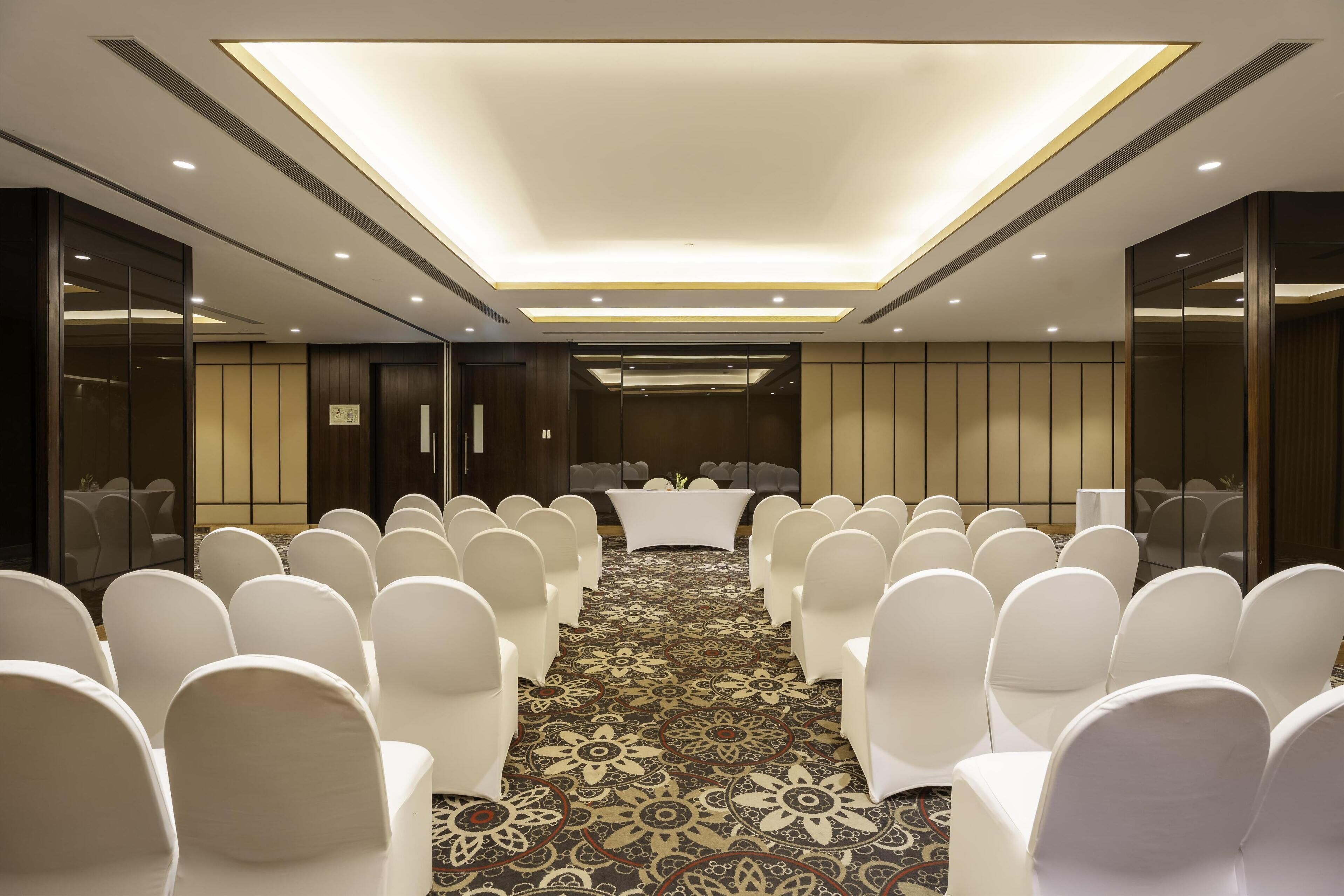 A conference room with rows of white chairs, a central table, and a patterned carpet.