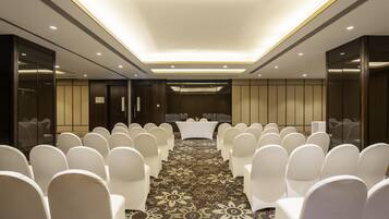 A conference room with rows of white chairs, a central table, and a patterned carpet.