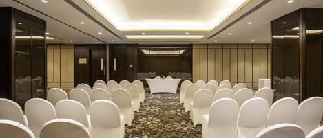 A conference room with rows of white chairs, a central table, and a patterned carpet.