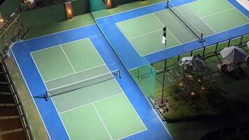 An outdoor tennis court with two courts, surrounded by a fence, and equipped with lighting.
