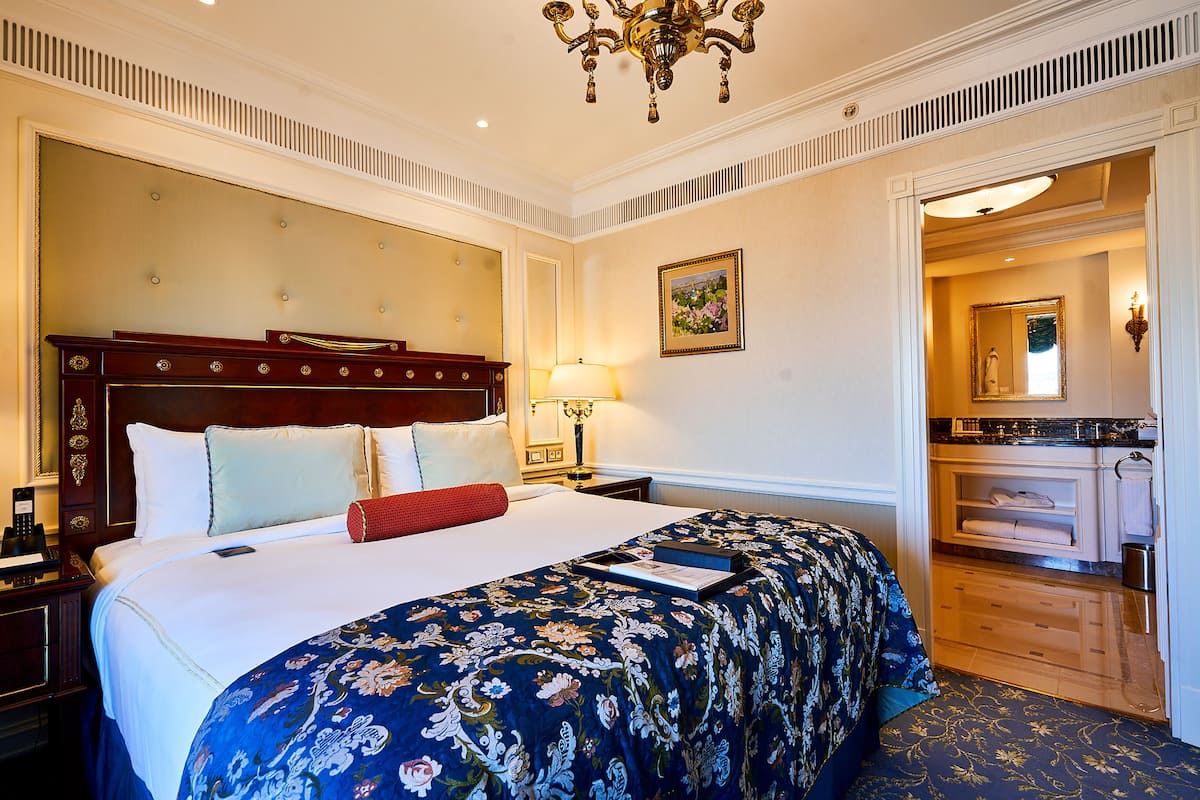 A hotel room with a large bed, a wooden headboard, a nightstand, a desk, and a bathroom visible through an open door.