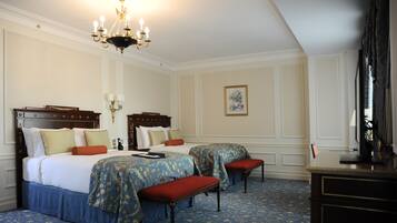 Habitación de hotel con dos camas, una araña, un escritorio y una alfombra estampada.