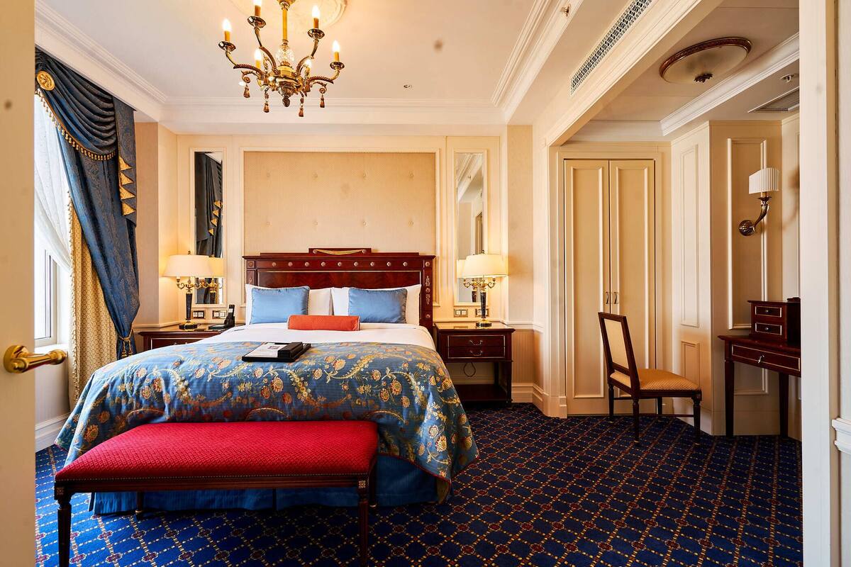 A hotel room with a large bed, a desk, a chair, and a chandelier.