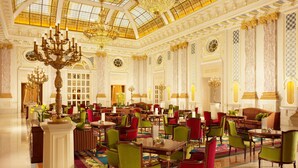 A grand hotel lobby with ornate chandeliers, a high-domed ceiling, and richly decorated walls.