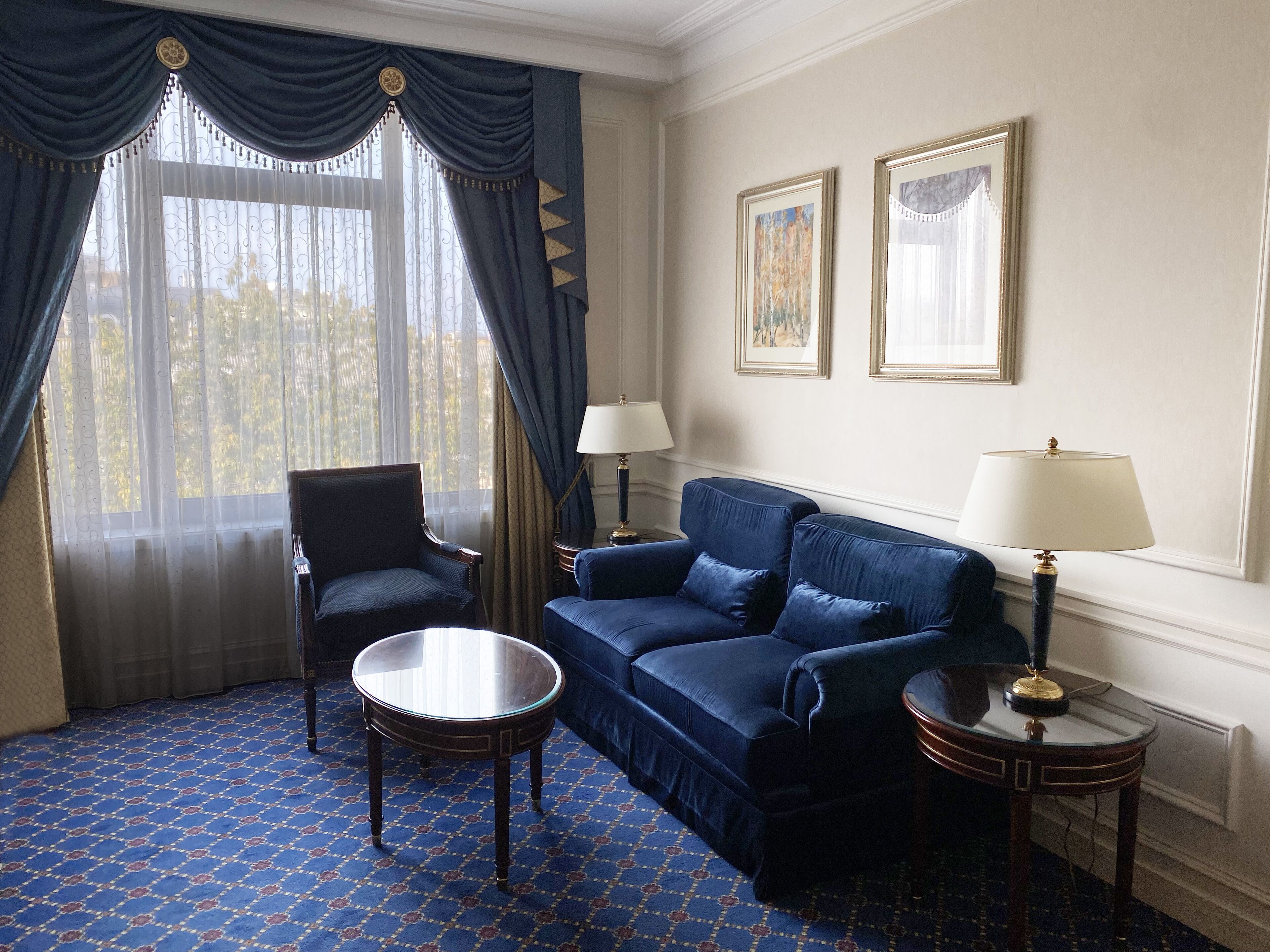 A room with a blue patterned carpet, a blue sofa, a round table, two lamps, and a chair.