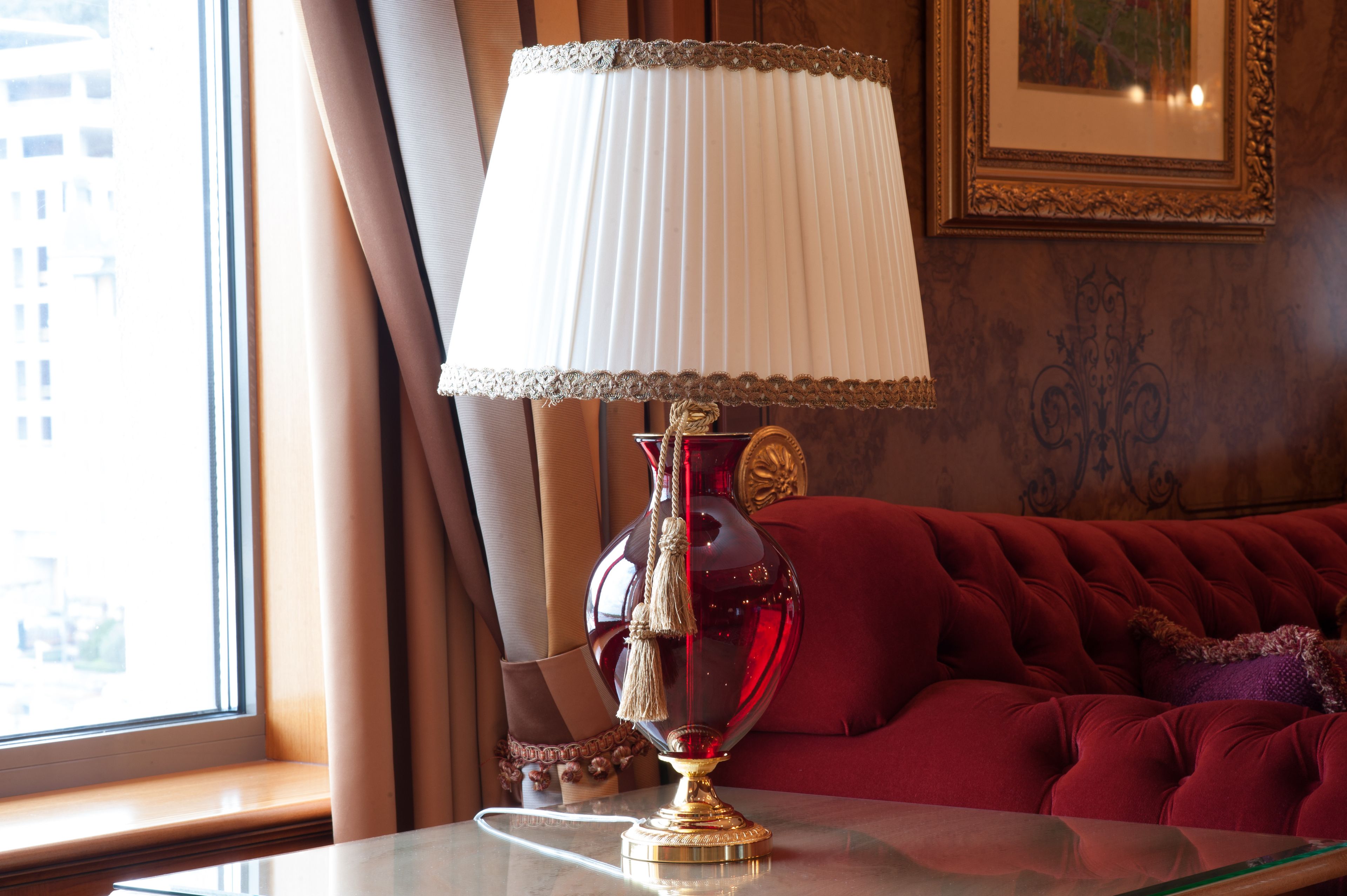 A room with a red sofa, a glass table with a red lamp, and a window with curtains.