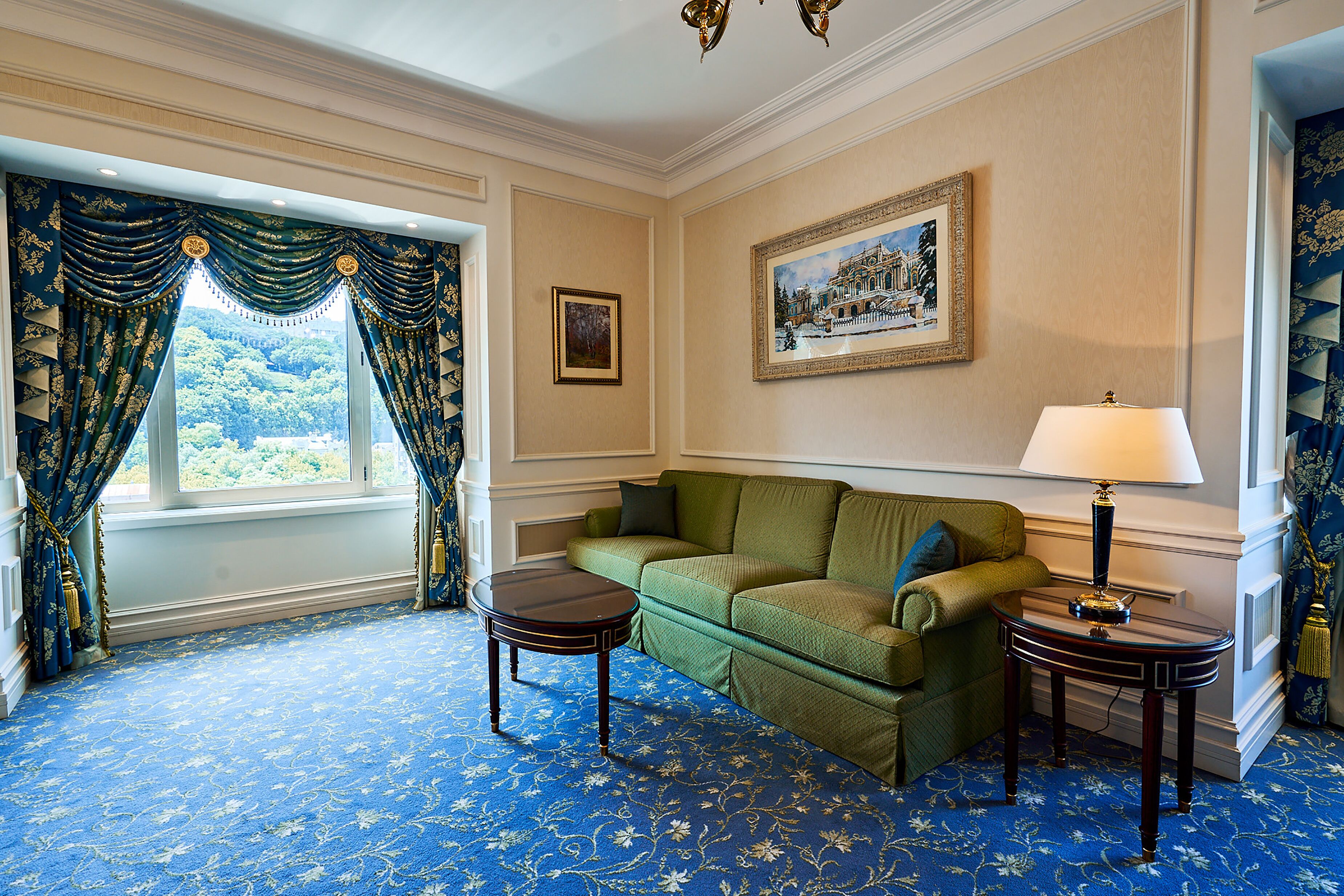 A room with a green sofa, two small tables, a lamp, and a framed picture on the wall.