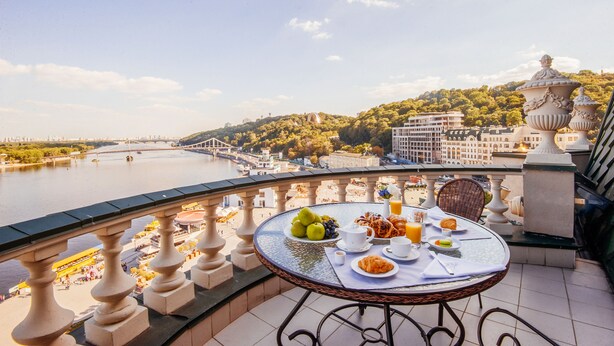 A balcony with a table set for breakfast overlooking a river and cityscape.