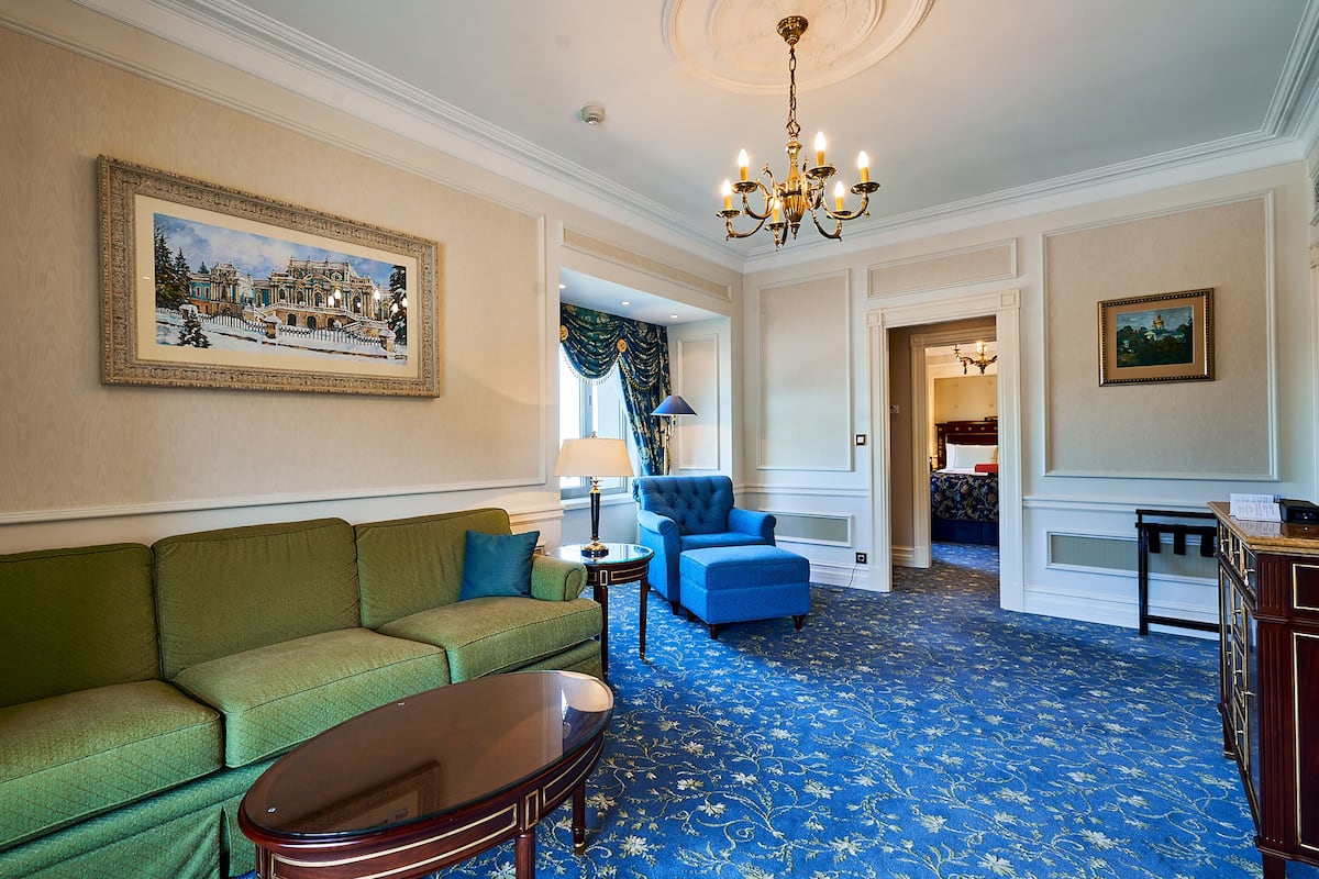 A room with a green sofa, a blue armchair, a wooden coffee table, and a chandelier.