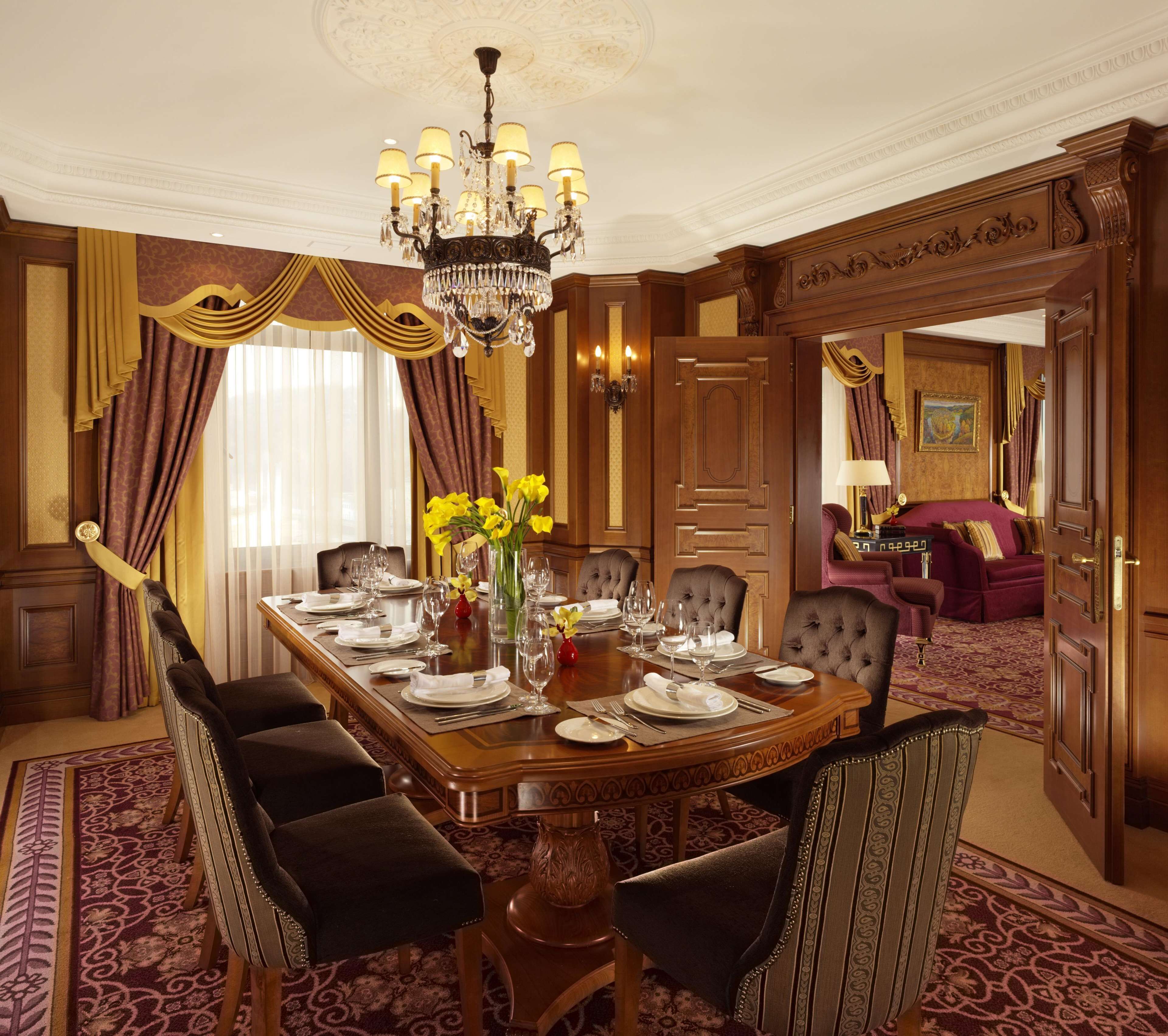 A formal dining room with a long table set for a meal, surrounded by upholstered chairs.