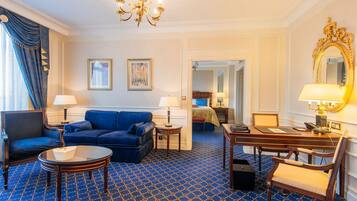 Een hotelkamer met een blauw kamerbreed tapijt, een blauwe bank, een houten bureau, een stoel, een lamp, een spiegel en een bed met een blauw hoofdeinde.