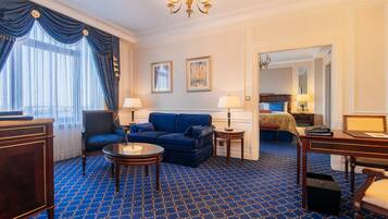 A hotel room with a blue patterned carpet, a blue sofa, two bedside tables with lamps, a wooden desk, and a chair.
