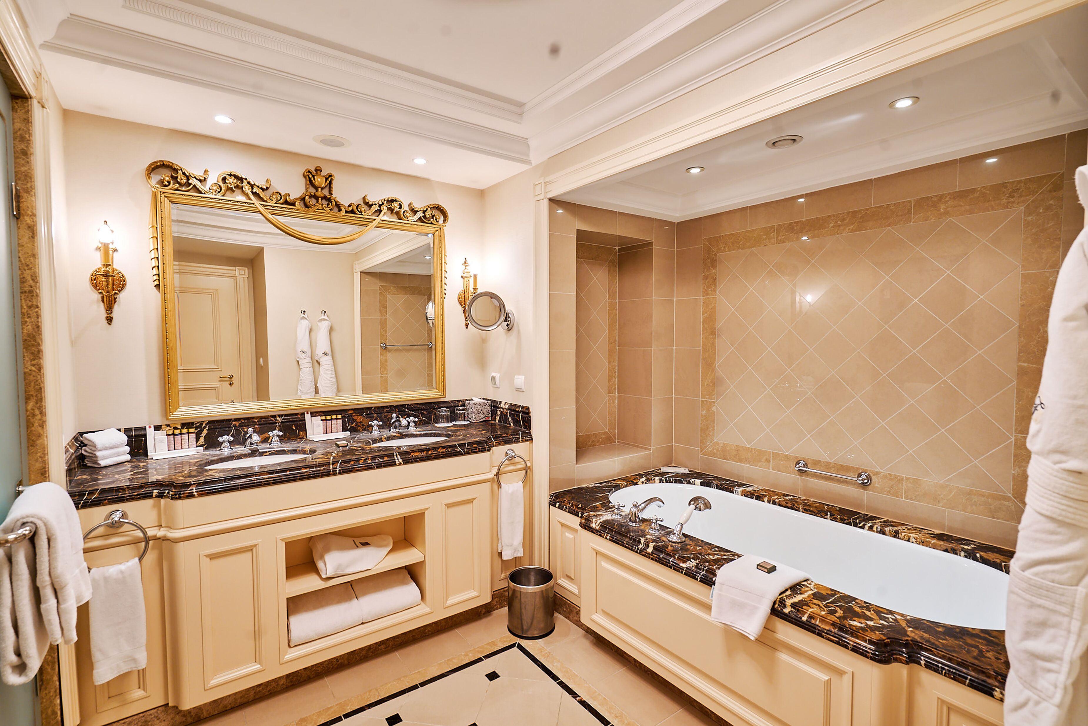 A luxurious bathroom with a marble vanity, a large bathtub, and a mirror with an ornate frame.