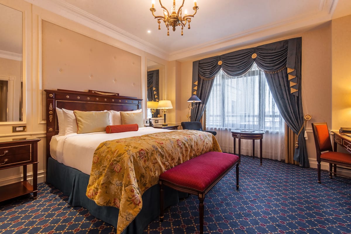 A hotel room with a large bed, a bench, a desk, and a chair.
