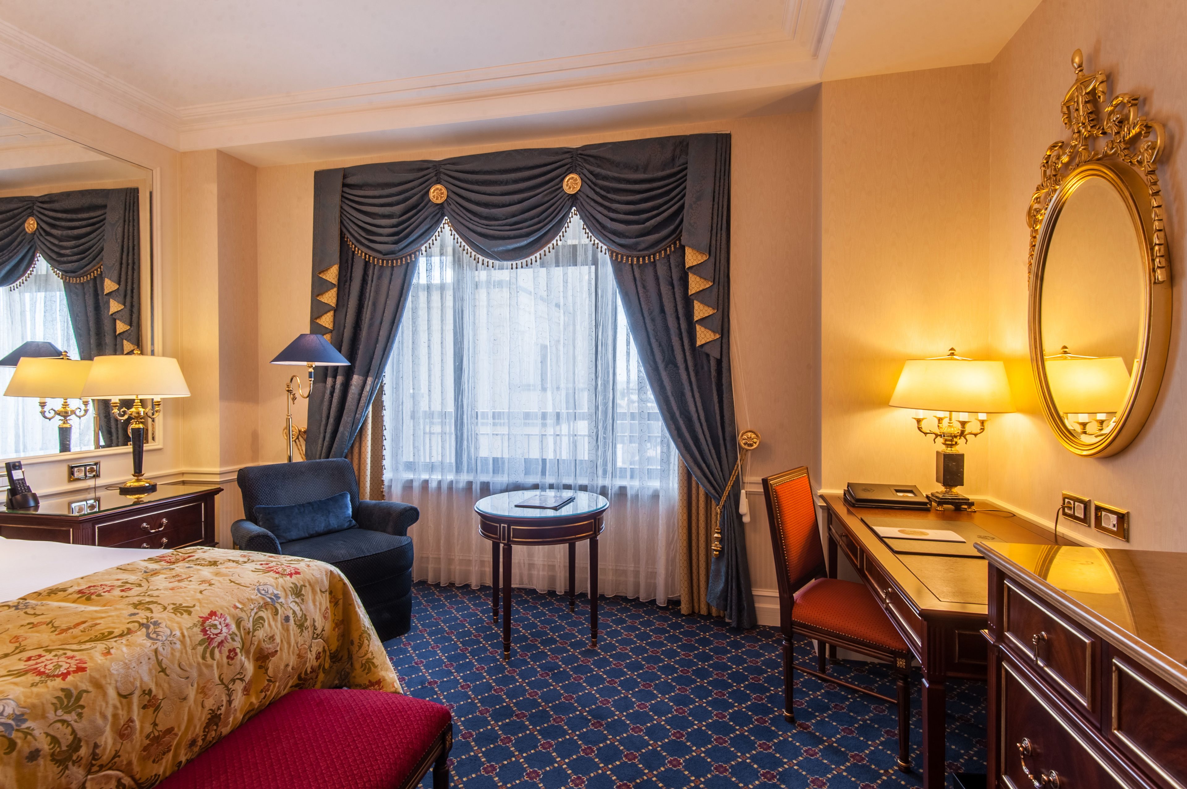 Une chambre d’hôtel comprenant un lit, un bureau, une chaise, une table ronde, une commode et un grand miroir.