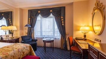 Une chambre d’hôtel comprenant un lit, un bureau, une chaise, une table ronde, une commode et un grand miroir.