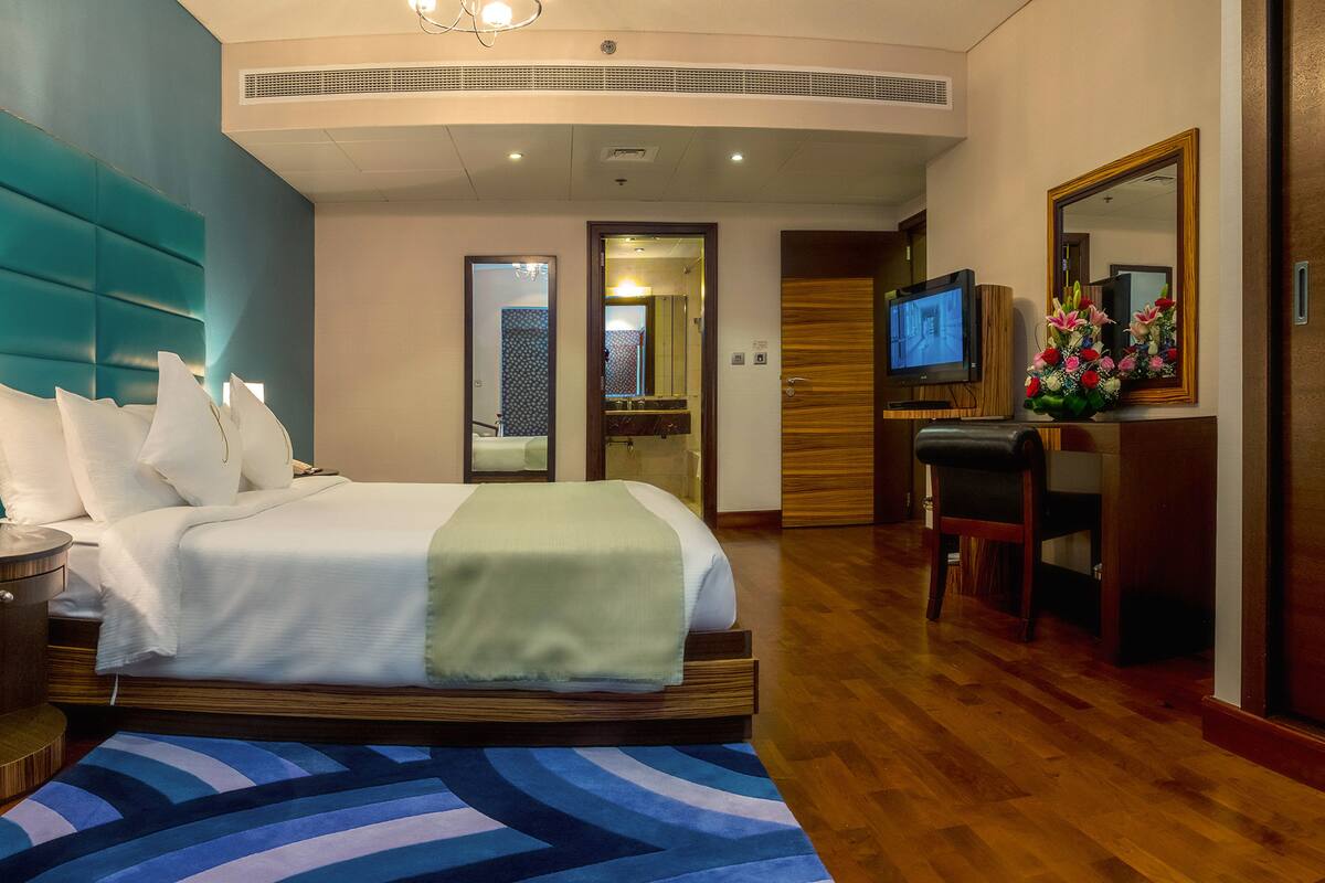 Una habitación de hotel con cama, escritorio, televisor y espejo.