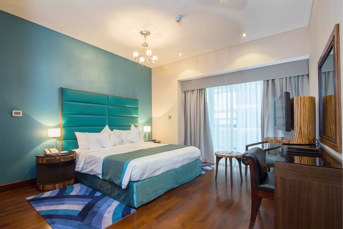 Una habitación de hotel con una cama grande, un escritorio, una silla, un televisor y una ventana con cortinas.