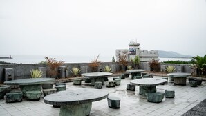 A terrace with multiple stone tables and benches, overlooking a body of water and a distant building. - Hotel Ocean (Hualien City)