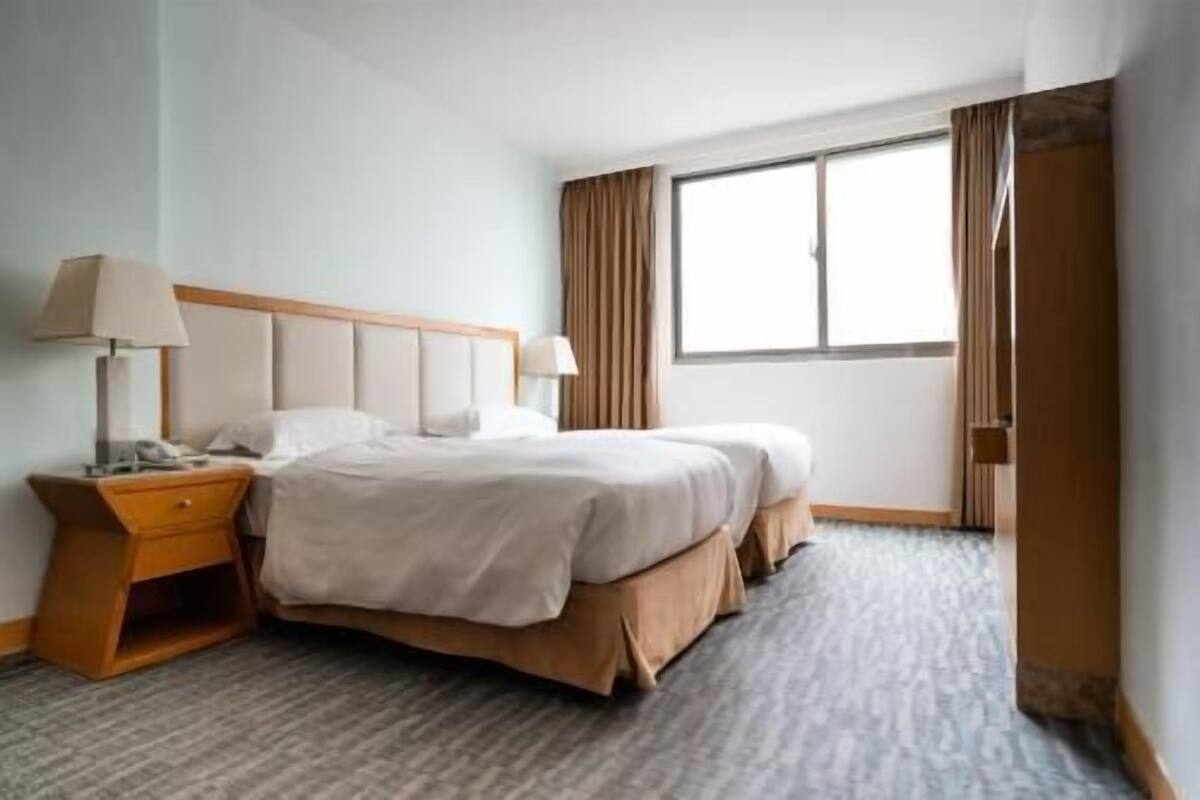 A hotel room with a bed, a nightstand, a lamp, a window with curtains, and a door.