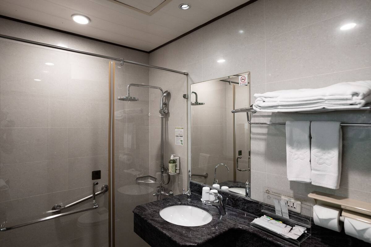 A modern bathroom with a glass shower enclosure, a sink with a marble countertop, and a mirror with a towel rack.