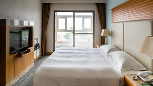 A hotel room with a large bed, a television, a desk with a telephone, and a view through a glass door. - Hotel Ocean (Hualien City)