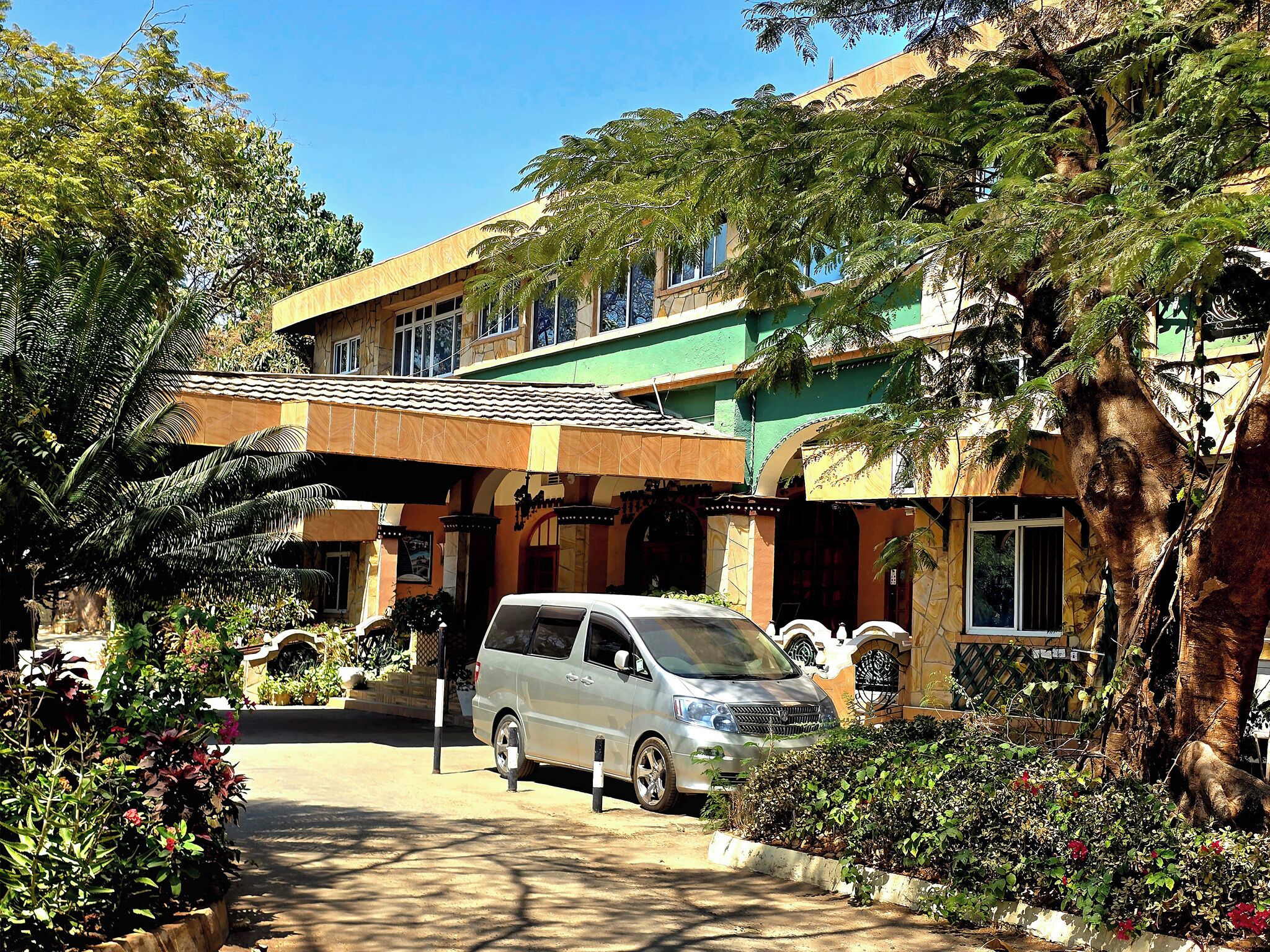 A building with a covered entrance, a parked car, and surrounding greenery.