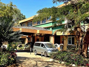 A building with a covered entrance, a parked car, and surrounding greenery.
