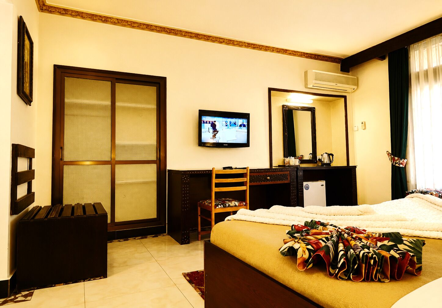 Habitación de hotel con cama, escritorio, silla, televisor y un ventanal con cortinas.