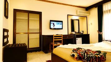 Habitación de hotel con cama, escritorio, silla, televisor y un ventanal con cortinas.