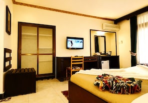 Habitación de hotel con cama, escritorio, silla, televisor y un ventanal con cortinas.