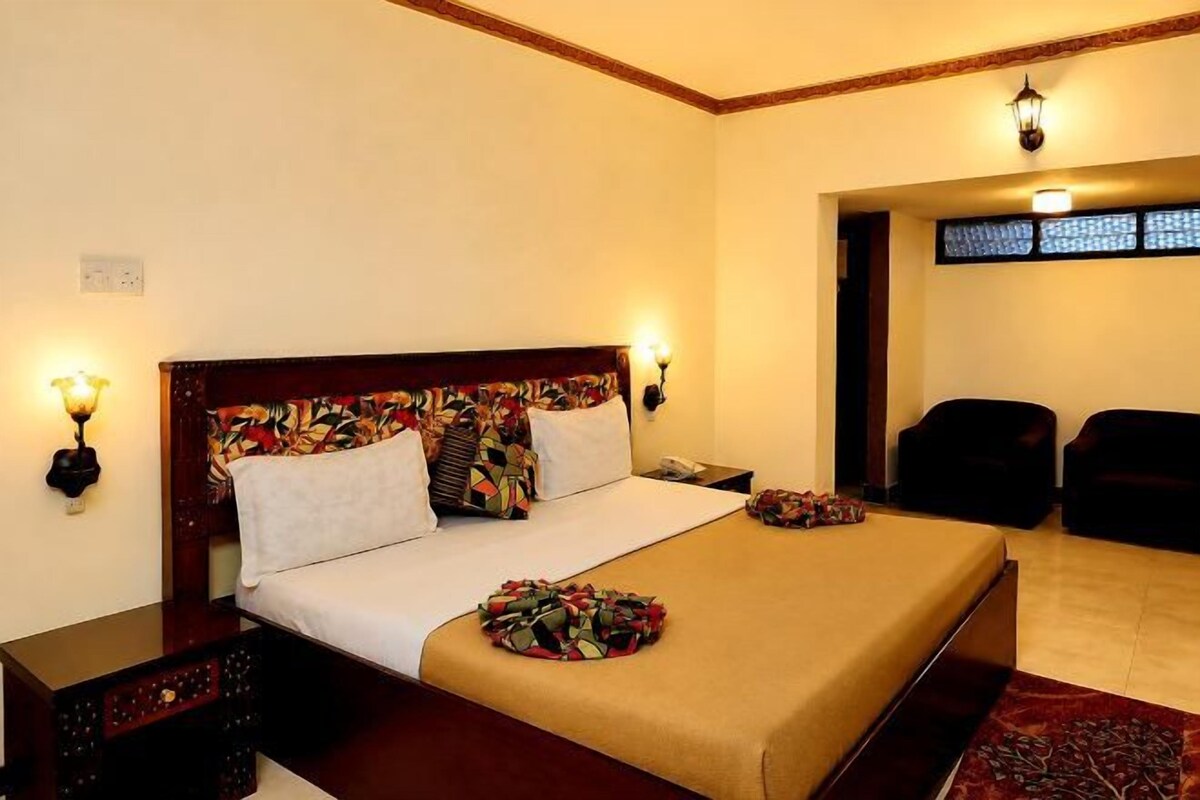Habitación de hotel con una cama grande, lámparas de noche, una mesita y vistas al exterior.