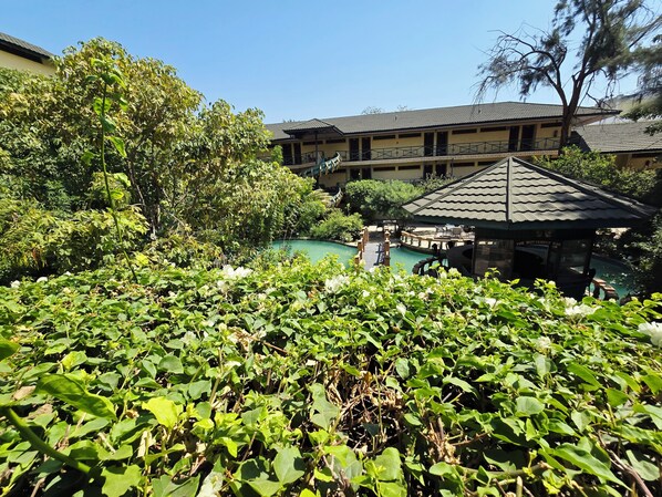 A pool area with a gazebo, lush greenery, and a building with a tiled roof. - New Dodoma Hotel (Dodoma)