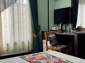A hotel room with a bed, a desk with a chair, a television, and a window with curtains. - New Dodoma Hotel (Dodoma)
