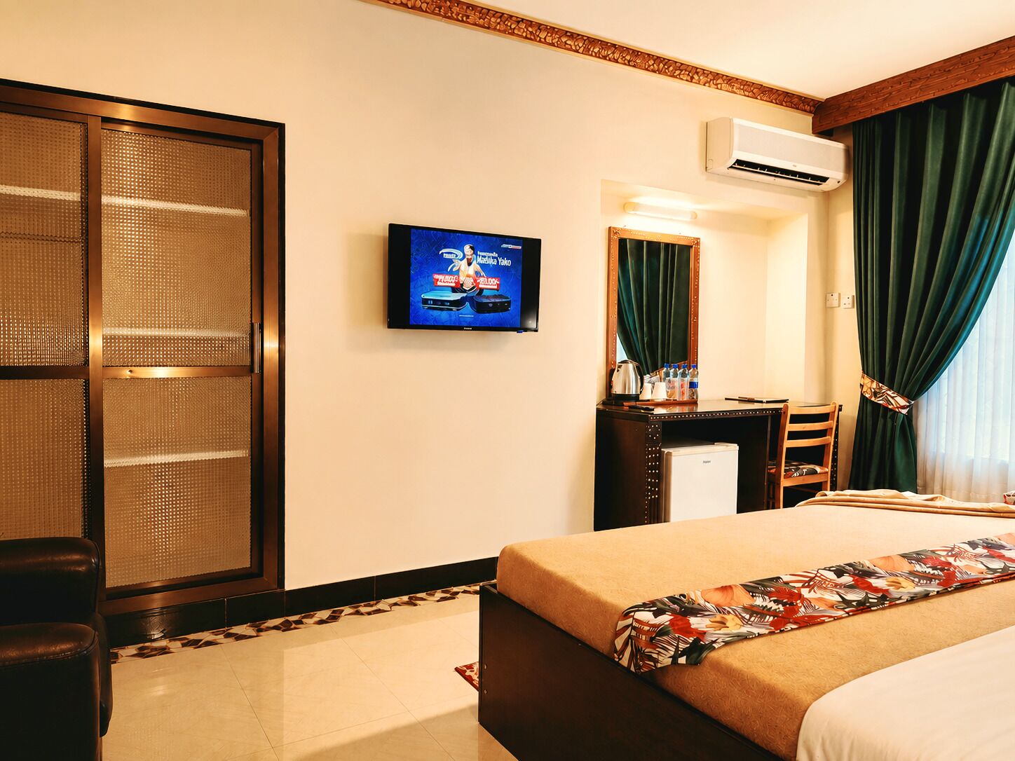 A hotel room with a bed, a desk, a television, a wardrobe, and an air conditioning unit.