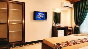 A hotel room with a bed, a desk, a television, a wardrobe, and an air conditioning unit.