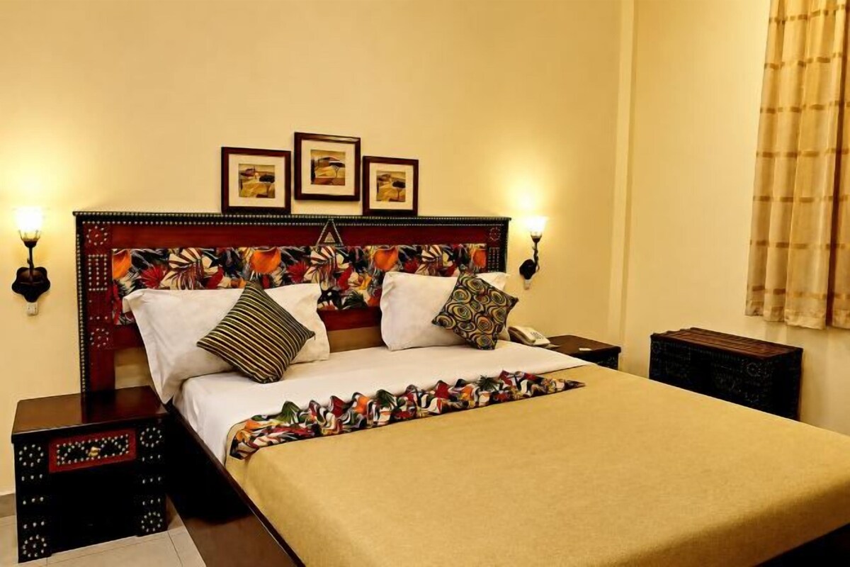 Una cama bien hecha con un edredón estampado, cabecera de madera con detalles decorativos y lámparas fijadas a la pared.